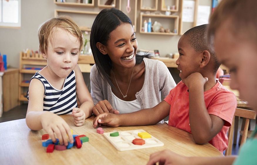 Teacher And Pupils Using Wooden Shapes In Montessori School